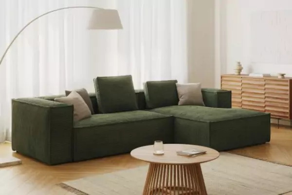 dunkelgrüne Eckcouch Blok aus Cord mit grünen und beigen Kissen. DAvor ein beiger Teppich mit einem runden Couchtisch.