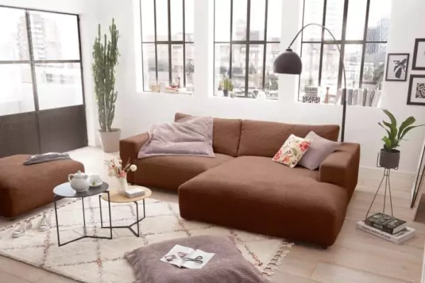 Rostrotes Ecksofa Lucia in Cordoptik auf einem beigen Franzenteppich mit rautemusterung und einem modernen Holzcouchtisch mit Metallfüßen