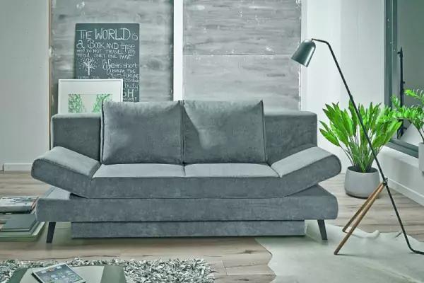 blaugraues Cord-Schlafsofa Sidney mit zwei farblich passenden Kissen mit einer schwarzen Stehlampe und einem weißen Blumentopf daneben