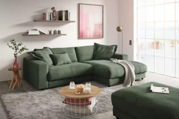 Ecksofa aus Cord Highend in grün mit passenden Kissen und einer weißen Decke auf einem hellgraumelierten Teppich. Davor steht ein Couchtisch mit holzplatte und Metallkorb
