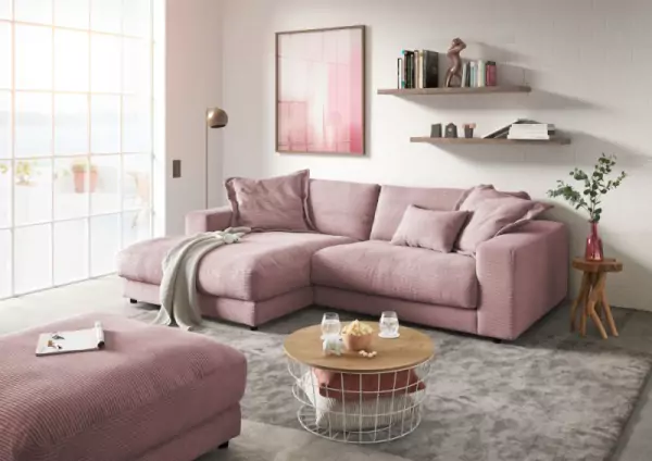 Ecksofa aus Cord Highend in altrosa mit passenden Kissen und einer weißen Decke auf einem hellgraumelierten Teppich. Davor steht ein Couchtisch mit holzplatte und Metallkorb