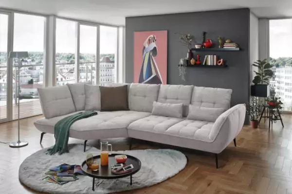 Cord-Wohnlandschaft Ticona in hellem grau auf einem runden Hochflorteppich in passendem Grauton und einem schwarzen Couchtisch. Auf dem Cordsofa liegen braune und graue Cordkissen