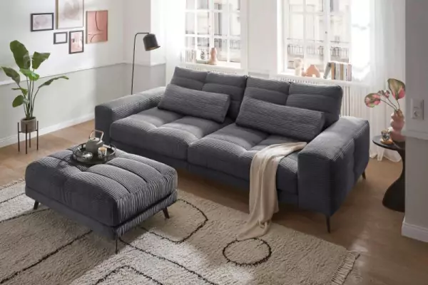 Beispielsofa für Breitcord-Optik. Helmond Cordsofa 3-Sitzer in dunkelgrau mit passendem Hocker auf einem beigen Teppich.