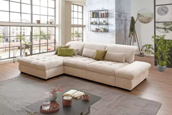 Beiges Ecksofa Vito Fulla in Cordoptik mit beigen und hellgrünen Kissen auf einem grauen Hochflorteppich