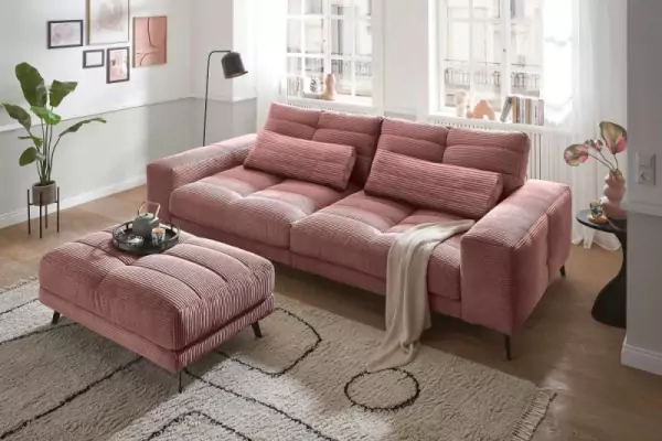 Helmond Cordsofa in Flamingo 3-Sitzer mit zwei Kissen und passendem Hocker auf hellbraunem Fransenteppich